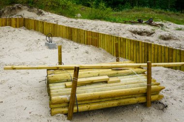 Kumlu toprakta ahşap bir istinat duvarı inşa ediliyor. Kereste direkleri ve yapısal elementler kullanıma hazır.
