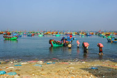 Mui Ne, Vietnam- 22 Mart 2025: İşçiler sığ sularda yüzen bir balıkçı teknesine büyük çuvallar yükler.