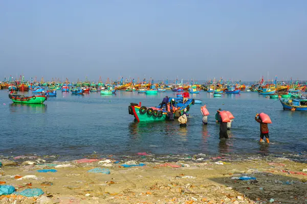 Mui Ne, Vietnam- 22 Mart 2025: İşçiler sığ sularda yüzen bir balıkçı teknesine büyük çuvallar yükler.