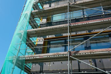 Termal yalıtım çalışmaları sırasında bina cephesinin yakın görüntüsü, yapı iskelesi ve yeşil güvenlik ağı görünür