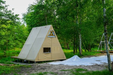 Suyun yakınındaki yeşil bir ormanda, yeni inşa edilmiş bir kareli kulübe eko-turizm konforu ve stili sunuyor.