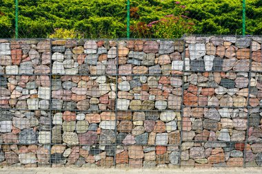 Çevre düzenlemesi ve erozyon kontrolü için kullanılan tel örgüdeki renkli doğal taşlardan yapılmış bir Gabion duvarına yakın plan.