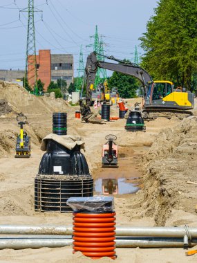 Altyapı geliştirme için elektrik hatları altında kazıcı, kamu hizmeti boruları ve rögar tesisleri bulunan inşaat sahası