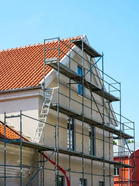 Güneşli bir günde binanın dış cephesi, kırmızı kiremitli çatısı ve inşaat ekipmanlarıyla yenileniyor.