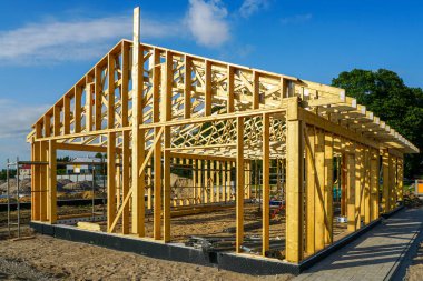 Güneşli bir günde inşaat halindeki modern ahşap ev iskeleti kirişleri, çatı kirişlerini ve ahşap yapıyı gösteriyor.