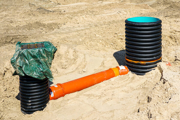 Sewer and rainwater manholes connected by orange pipe on a sandy construction site, part of drainage and utility infrastructure installation