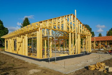 ICF temeli üzerine inşa edilmiş ahşap bir ev iskeleti. İnşaat iskelesi, kereste ve aletler açık bir yaz gününde görünür.