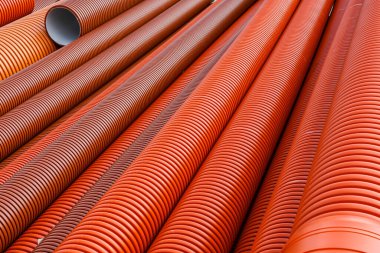 Açık havada, kanalizasyon, drenaj ve inşaat projelerinde kullanılan büyük turuncu kıvrımlı plastik borular yığını.