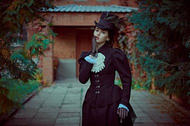 19. yüzyılın zarif genç hanımı tuğla bir Victoria evinin bahçesinde yürüyor. 19. yüzyılın sonları ve 20. yüzyılın başlarına ait tarihi yeniden yapılanma..