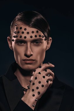 Moda konsepti. Siyah ceketli yakışıklı bir adamın portresi. Yüzünde ve kolunda siyah bir arka planda metal çiviler var..