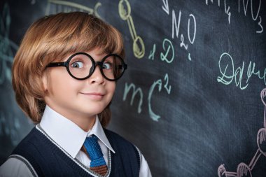 Eğitim. Güzel bir okul üniforması ve gözlüklü yakışıklı bir çocuk mutlu bir gülümsemeyle kimyasal formüllerle tahtada duruyor. Akıllı çocuklar..  