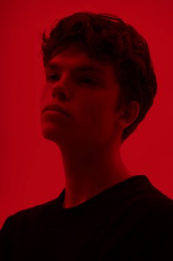 Ergenler ve iç dünya. Dalgalı siyah saçlı, yüzünde depresif bir ifadeyle dalgın dalgın bakan yakışıklı bir adamın portresi. Kırmızı arkaplanda stüdyo çekimi. 