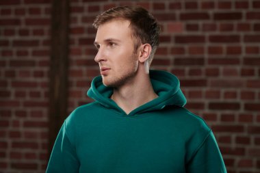 Tuğla duvarın arkasında duran şık bir kapüşonlu genç adamın portresi. Genç insanlar, aktif yaşam tarzı.