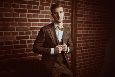 Çatı katı tarzı bir odada, üç parçalı şık takım elbiseli, saygıdeğer bir gencin portresi. Erkek modası.