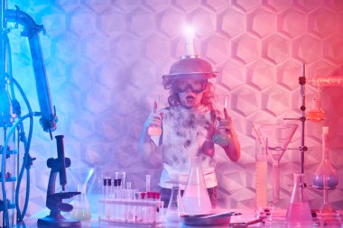 Bilim deneyleri ve çocuklar. Gözlüklü ve kafasında garip bir buluş olan sevimli, şaşırmış bir kız laboratuarda kimyasal deneyler yapıyor. Eğitici kavram. 