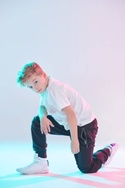 Hip-hop dansçısı. Stüdyoda dans eden havalı break dansçı çocuk beyaz arka planda karışık renkli ışıklandırmada dans ediyor. Spor ve aktiviteler. Modern dans stili. 