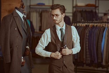 Yakışıklı kahverengi takım elbiseli saygıdeğer bir esmer adamın portresi şık kemerli bir erkek giyim mağazasında duruyor. Erkeklerin iş modası.