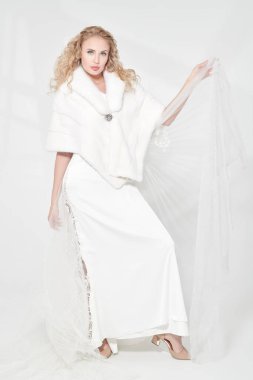 Pahalı bir gece elbisesi ve vizon peleriniyle kıvırcık sarı saçlı zarif genç bayan. Lüks bir şekilde. Güzellik, moda portresi. Gelinlik. Tam boy çekim.