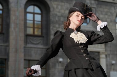 Şehir caddesinde yürüyen siyah elbiseli ve şapkalı güzel bir hanımın portresi. 19. yüzyılın sonları - 20. yüzyılın başları.