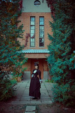 19. yüzyılın zarif genç hanımı tuğla bir Victoria evinin bahçesinde yürüyor. 19. yüzyılın sonları ve 20. yüzyılın başlarına ait tarihi yeniden yapılanma..