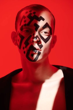 Yüzünde QR kodu olan genç bir adamın sanat portresi, kırmızı ışıkta ve kırmızı arka planda yanan kameraya düşmanca bakıyor. QR kod kavramı, koronavirüse karşı aşı. 