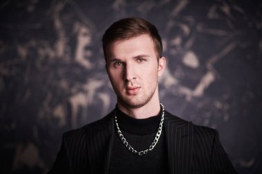 Arkaplanda duran siyah kazaklı ve ceketli çekici bir gencin portresi. Erkek modası.