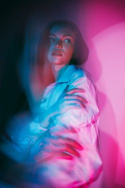 Beyaz gömlekli, uzun saçlı güzel bir kızın portresi. Kendine sarılıyor ve başka tarafa bakıyor. Mavi ve kırmızı renkte bulanık stüdyo portresi.