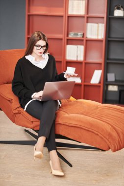 Güzel bir iş kadını, modern bir ofiste bir koltukta dizüstü bilgisayarla çalışıyor. İş ve iletişim. Modern iç mekan, mobilyalar. Modern teknolojiler.