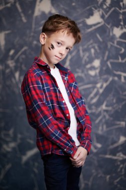 Ekose gömlekli, yakışıklı bir çocuğun portresi grunge arka planda sakince duruyor. Çocuk modası.