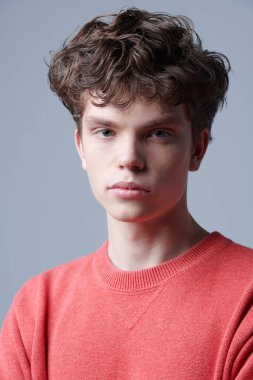 Gri arka planda duran kırmızı kazaklı yakışıklı bir adamın portresi. Erkeklerin gençlik modası. 