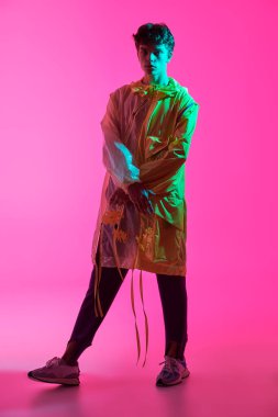 Yüksek moda çekimi. Yaratıcı tasarımcı kıyafetleriyle stüdyoda poz veren yakışıklı bir erkek modelin portresi. Parlak giysi renkleri. Pembe arkaplanda tam boy çekim.