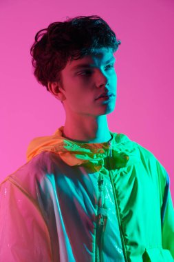 Tasarımcı koleksiyonundan parlak gençlik kıyafetleri. Parlak pembe bir arka planda şık tasarımcı kıyafetleriyle siyah dalgalı saçlı yakışıklı bir erkek model. Yüksek moda çekim. 