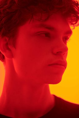 Turuncu arka planda, kapkara saçlı yakışıklı bir adamın, üzgün bir ifadeyle kırmızı ışıkta yüzünü çevirmesini yakından çek. Ergenler ve akıl sağlığı.