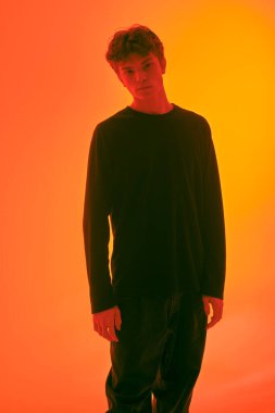 Kırmızı ışıklandırmalı, turuncu arka planda duran kapkara saçlı yakışıklı bir adamın stüdyo fotoğrafı. İnsanlar, duygular. 