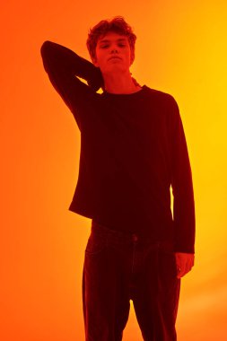 Dalgalı kahverengi saçlı yakışıklı huysuz bir adam turuncu arka planda kameraya kırmızı ışıkla bakıyor. Ergenler ve duygular. 