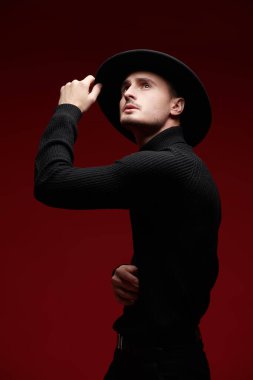 Siyah balıkçı yaka kazaklı ve kırmızı stüdyo arka planında poz veren şık esmer bir adam. Erkek güzelliği ve tarzı. 