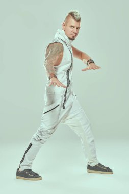 Mohawk ve dövmeleri olan yakışıklı bir punk rock müzisyeni hafif bir stüdyoda poz veriyor. Siber punk stili. 