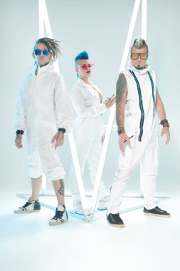 Üç karizmatik müzisyenden oluşan rock grubu neon ışıklar arasında beyaz konser kostümleri içinde poz veriyorlar. Gelecekçi mekan ve cybepunk tarzı. Gençlik alternatif kültürü. Tam boy portre.