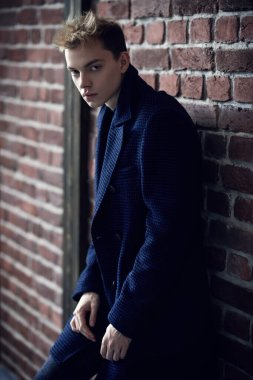 Hayat, insanlar ve duygular. Palto giymiş genç bir adamın portresi, tuğladan bir duvara yaslanmış ve ne yazık ki kameraya bakıyor.. 