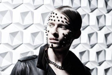 Agresif bir moda. Siyah deri ceketli, beyaz teknoloji arka planında metal çiviler olan vahşi bir gencin portresi..