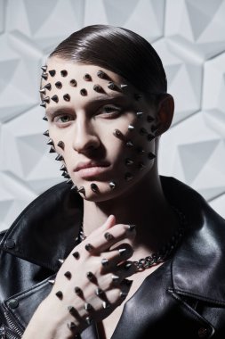 Agresif bir moda. Siyah deri ceketli, beyaz teknoloji arka planında metal çiviler olan vahşi bir gencin portresi..