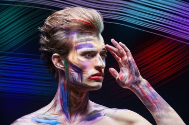 Sanat, moda ve vücut boyama. Renkli boyalı yüzü olan yakışıklı bir sarışının portresi renkli neon çizgileri olan siyah bir arka planda duruyor..