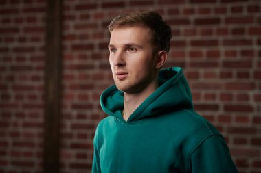 Tuğla duvarın arkasında duran şık bir kapüşonlu genç adamın portresi. Genç insanlar, aktif yaşam tarzı.