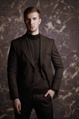 Erkek modası. Klasik siyah takım elbise ve siyah süveter giymiş yakışıklı bir adam grunge arka planda poz veriyor. Zarif stil. 