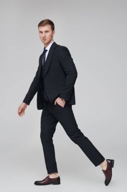 Klasik siyah üç parçalı takım elbiseyle poz veren yakışıklı bir adamın moda fotoğrafı. Beyaz arka plan. İş stili. Erkek modası. Başarılı insanlar..