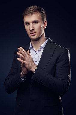 Klasik siyah takım elbiseli ve beyaz gömlekli şık bir adam koyu mavi arka planda poz veriyor. Akşam stili. Erkek modası.