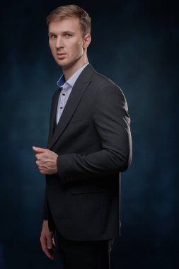 Klasik siyah takım elbiseli ve beyaz gömlekli şık bir adam koyu mavi arka planda poz veriyor. Akşam stili. Erkek modası.