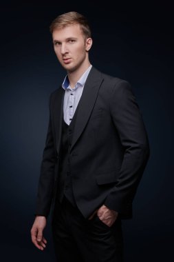 Erkek modası. Siyah takım elbiseli, beyaz gömlekli yakışıklı bir adam koyu bir arka planda poz veriyor. Şık bir akşam stili.. 