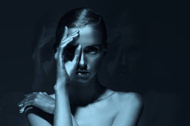 Metalik gümüş tenli, kollarıyla zarif poz veren sevimli bir bayan model. Karanlık arka plan. Vücut boyama, vücut sanatları. Moda ve sanat.