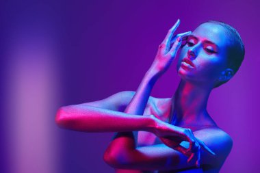 Parlak gümüş vücut boyasıyla kaplı güzel bir kızın sanat portresi. Kolları neon mavisi ve pembe ışıkla sanatsal poz veriyor. Güzellik ve kozmetik konsepti. Vücut boyama. Boşluğu kopyala.